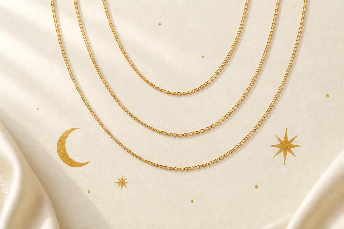Three plain gold chains above hand-painted gold moon and stars on ivory paper