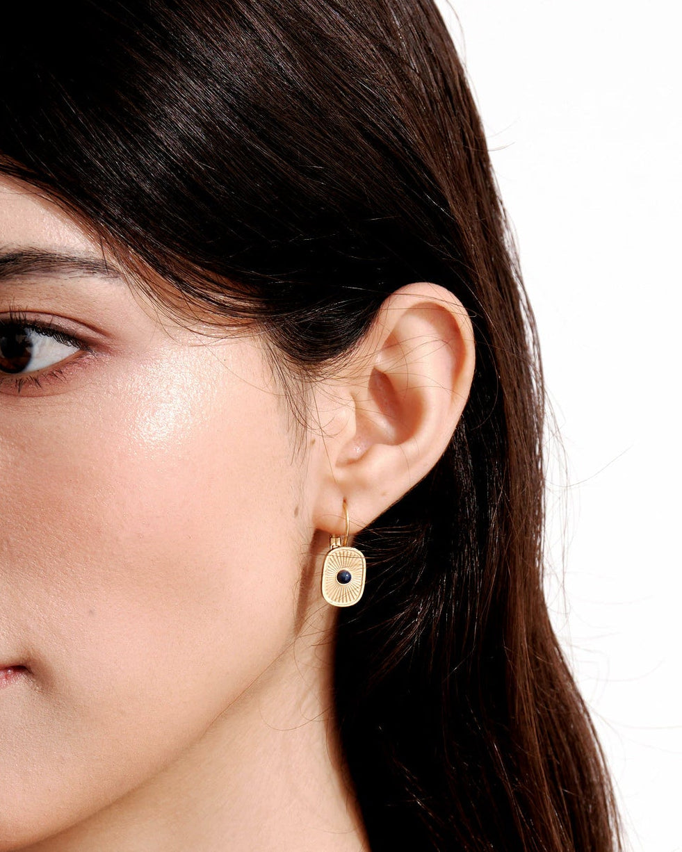 Aurora Talisman Huggie Earrings worn in profile, showing the curved fastening and blue-centered gold drop beside the ear.