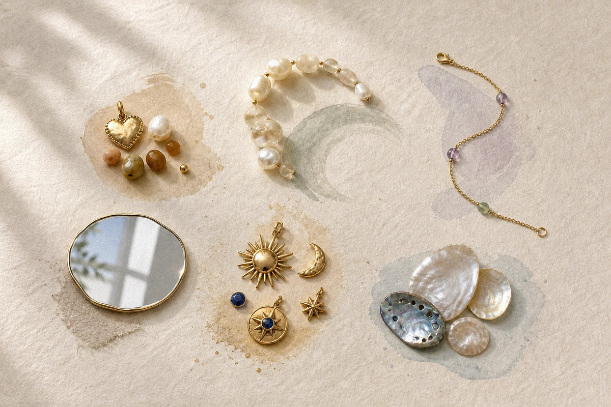 Gold heart, pearl arc, fine chain, mirror, celestial charms, and shells arranged on ivory paper