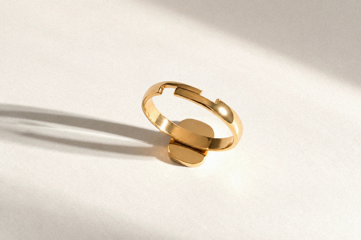 Gold-tone adjustable ring viewed from behind, with its band opening visible on a sunlit ivory surface