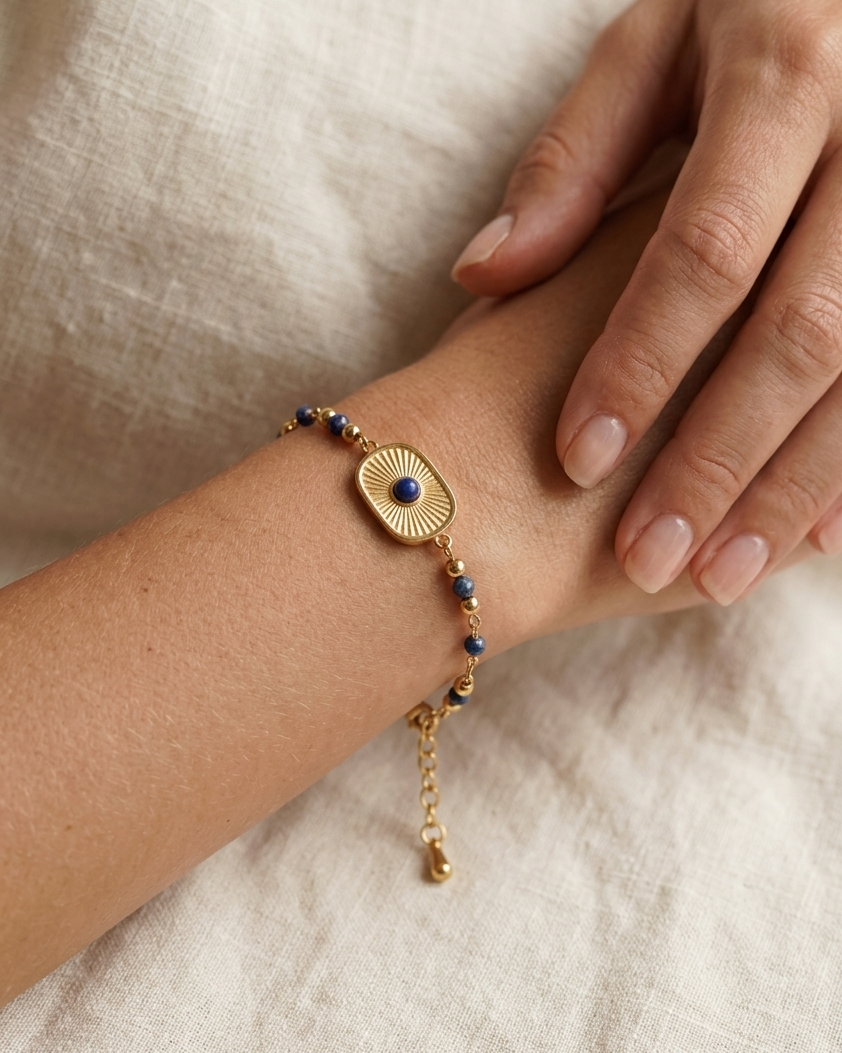 Model wearing Lapis Lazuli Sunburst Bracelet with blue lapis beads and a gold sunburst charm on wrist over soft white fabric