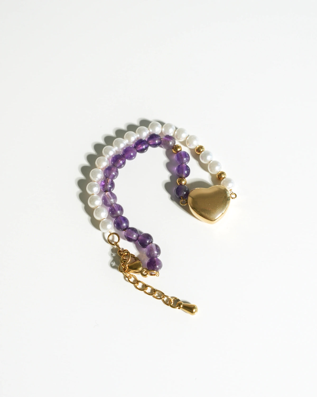 Radiant Harmony Heart Bracelet laid flat on a cream background with amethyst beads, white pearls, and a gold heart charm