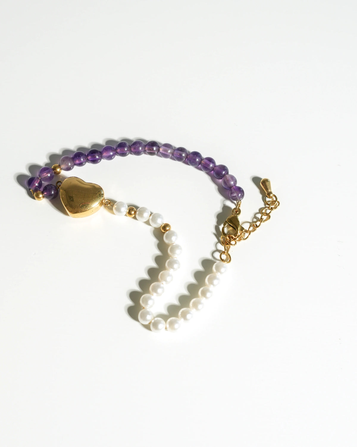 Close-up of natural purple Amethyst beads and white pearls on a delicate gold wellness bracelet.