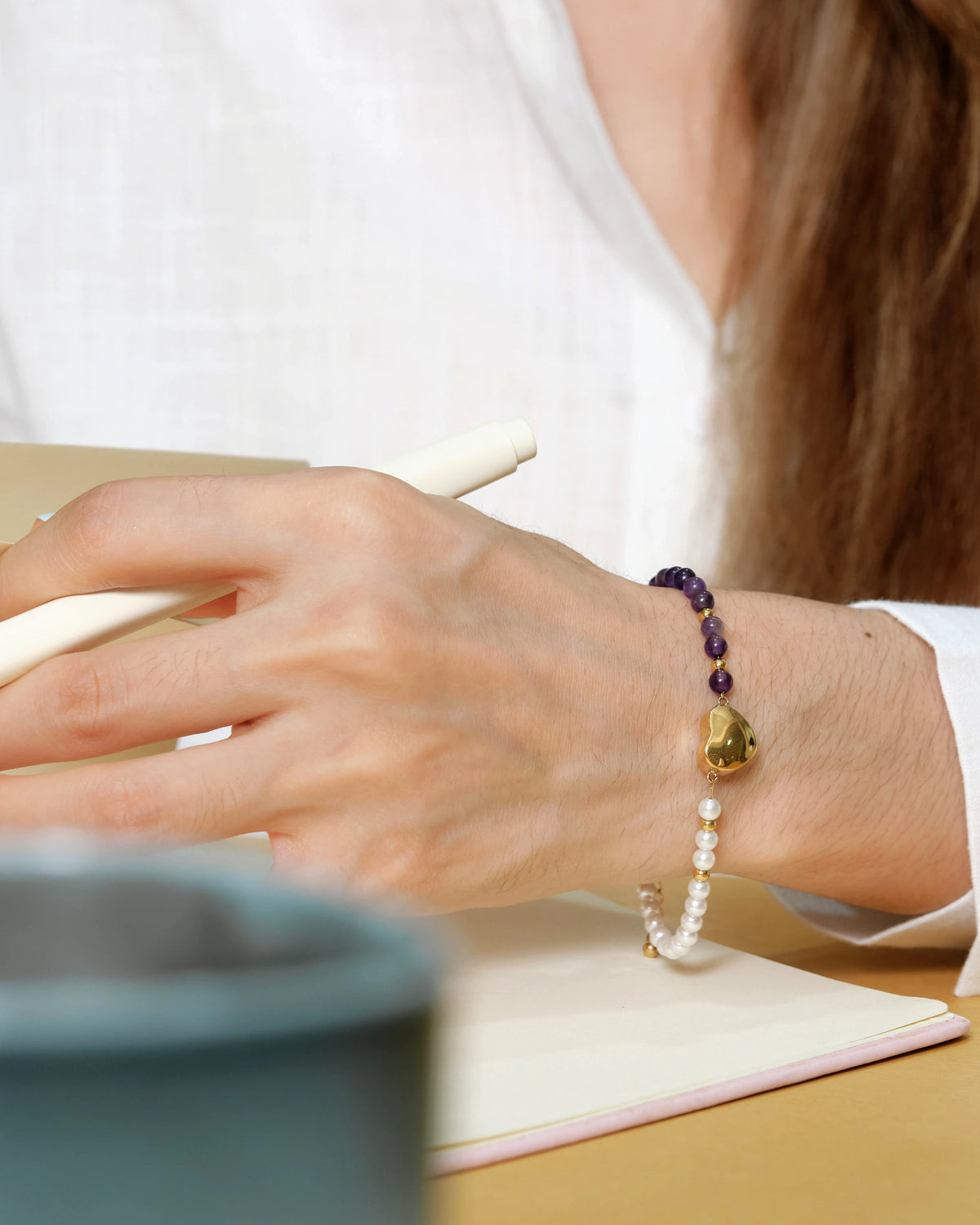 Model wearing the Amity Heart Bracelet while writing at a desk