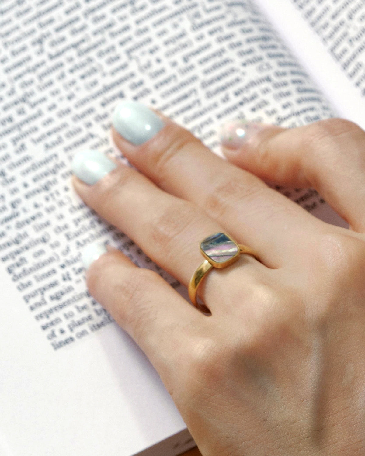 Tidal Stone Ring worn on a hand resting on an open book