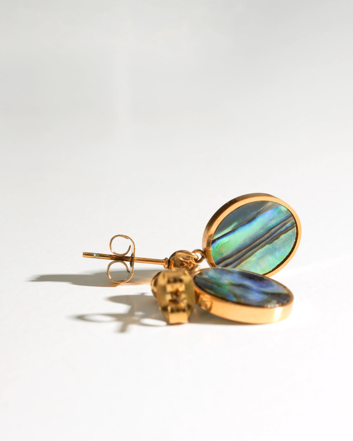 Close-up of Tidal Stone Stud Earrings with round iridescent shell inlays