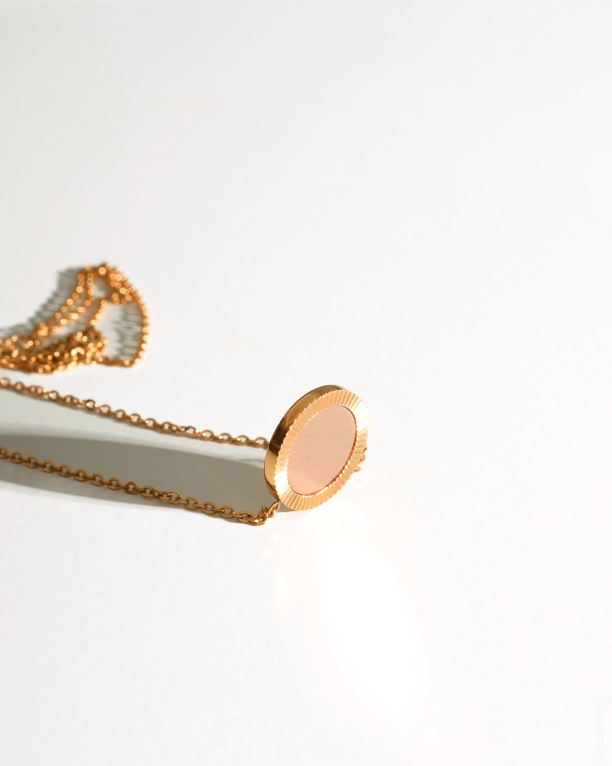Gold Reflection Pendant Necklace laid flat on a cream background