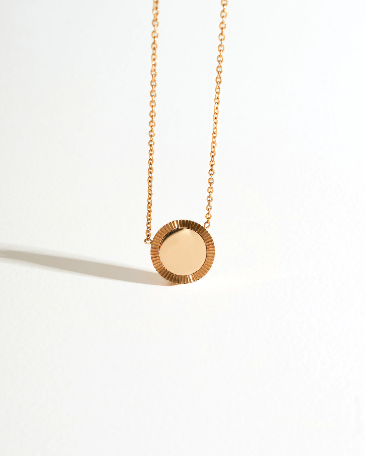 Gold Reflection Pendant Necklace lying on a white surface with circular mirror pendant