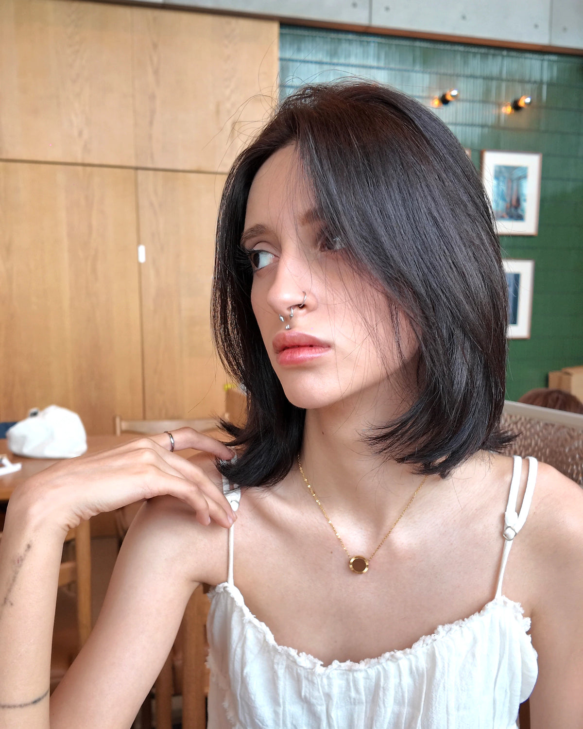 Lifestyle portrait of a model wearing the Gold Reflection Pendant Necklace in a café