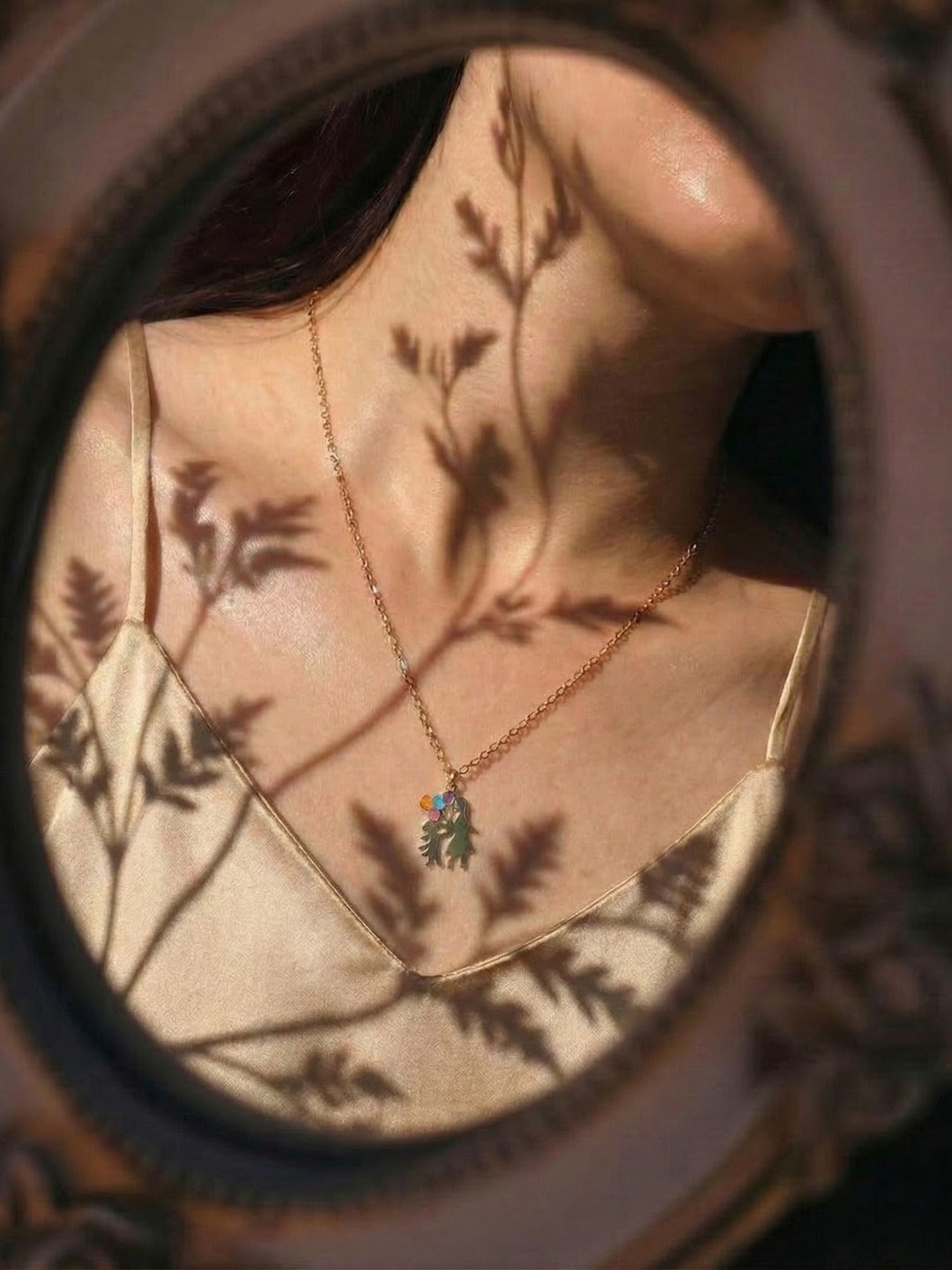 A necklace seen through a mirror with soft botanical shadows.